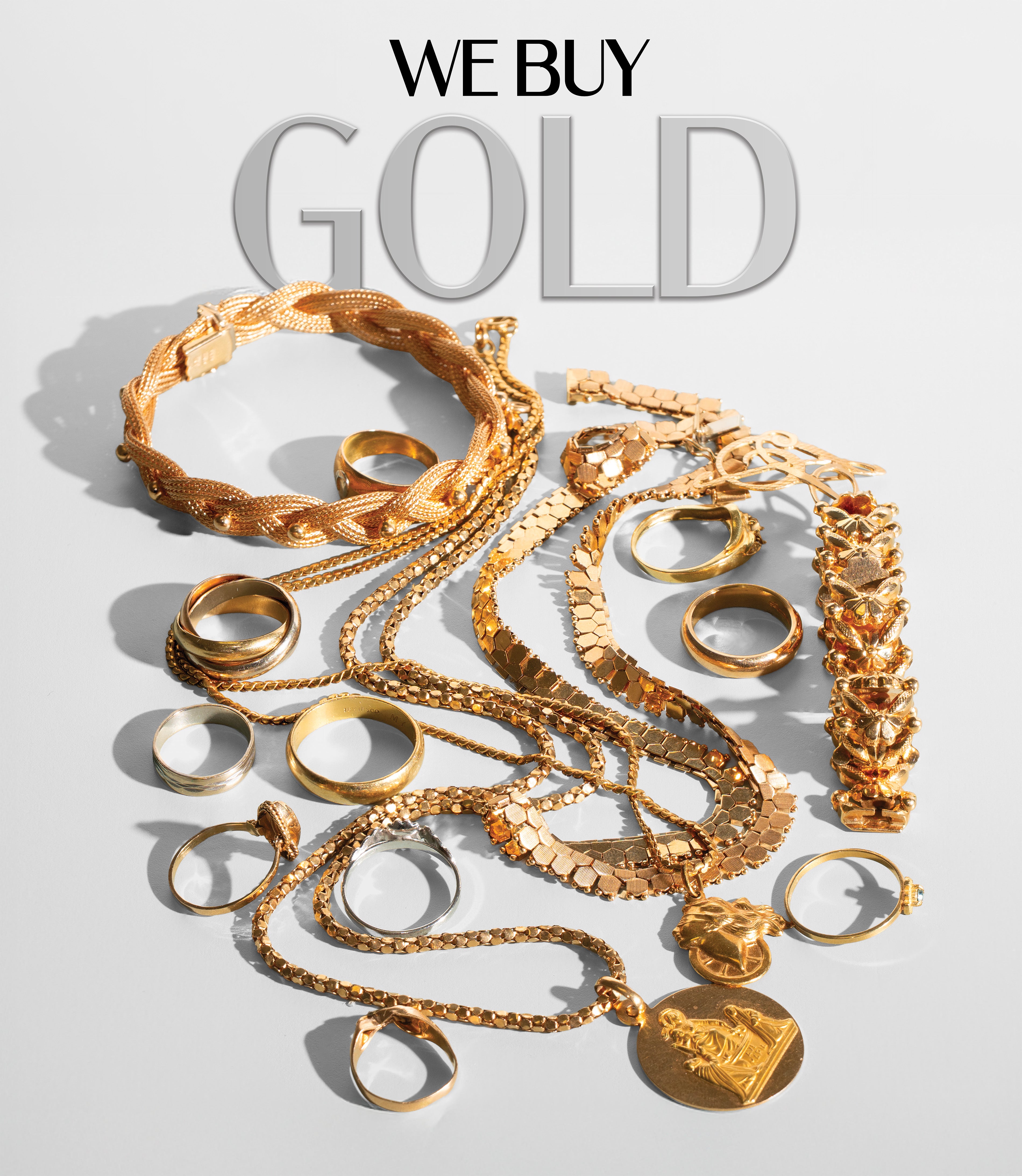 A collection of gold jewelry pieces, including rings, chains, bracelets, and necklaces, arranged on a light gray reflective surface with the text 'WE BUY GOLD' above them.